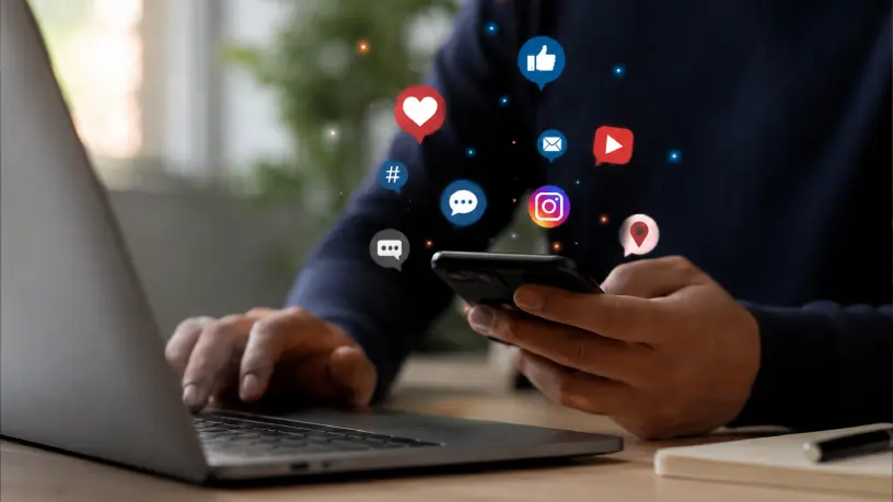 Pessoa utilizando notebook e smartphone com ícones de redes sociais e interações digitais. A imagem representa o fortalecimento da autoridade digital por meio do engajamento, da comunicação online e da presença ativa nas plataformas digitais.