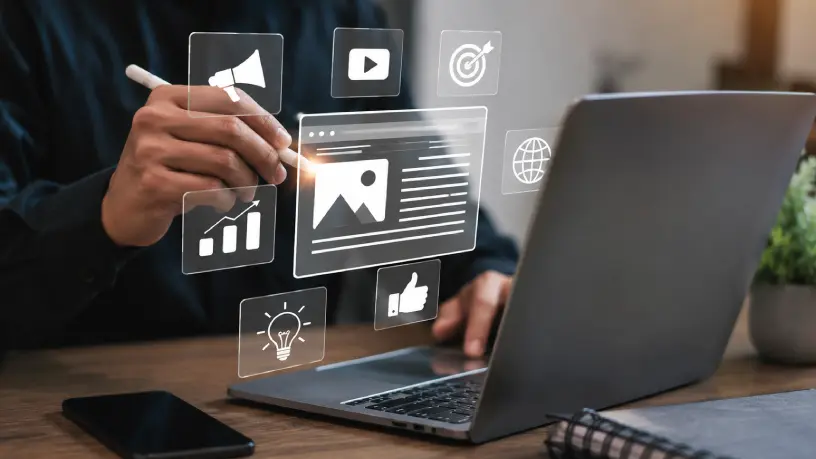 Imagem de profissional criando produção de conteúdo em notebook, com ícones de mídia, marketing digital, crescimento, alcance, engajamento e objetivos, representando estratégia de conteúdo para fortalecer a autoridade digital e a presença online da empresa.